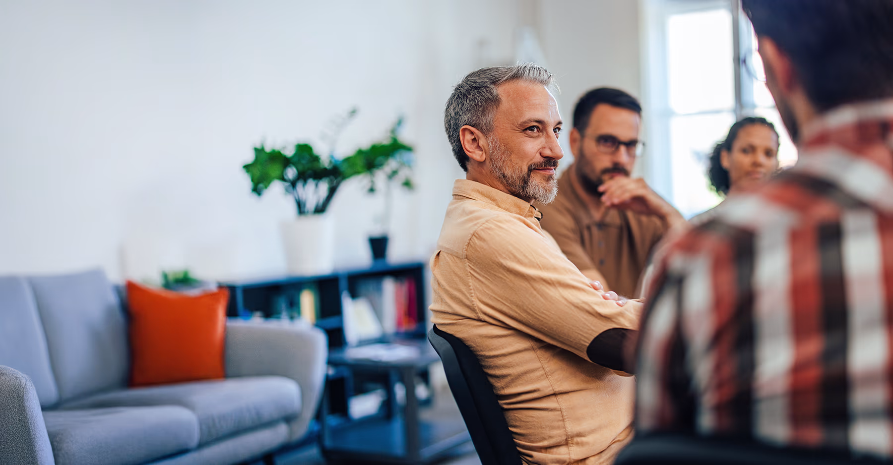 Middle-aged man with gray hair listening attentively during a group discussion in a modern office setting
